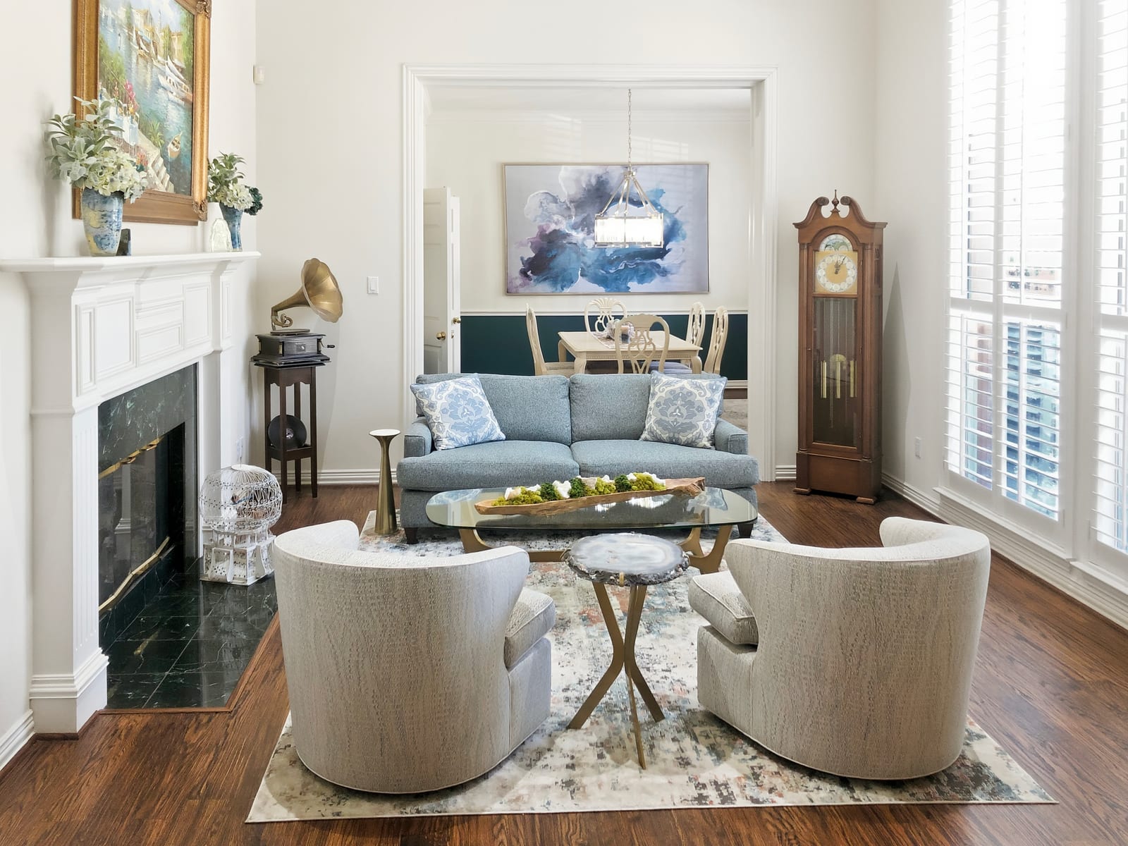 Living room with a white fireplace, blue sofa and cream swivel chairs opening to the dining room